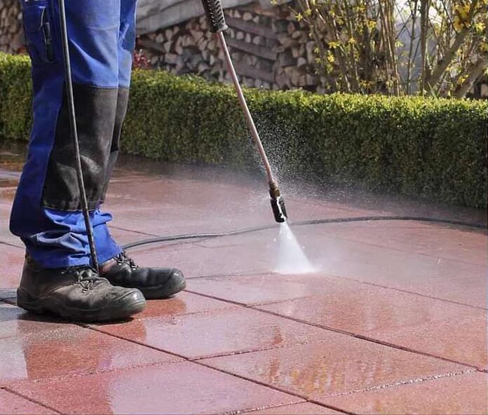 Total Property Management Services team member pressure-washing tiled surface as part of outdoor cleaning and sanitation service in Guyana.