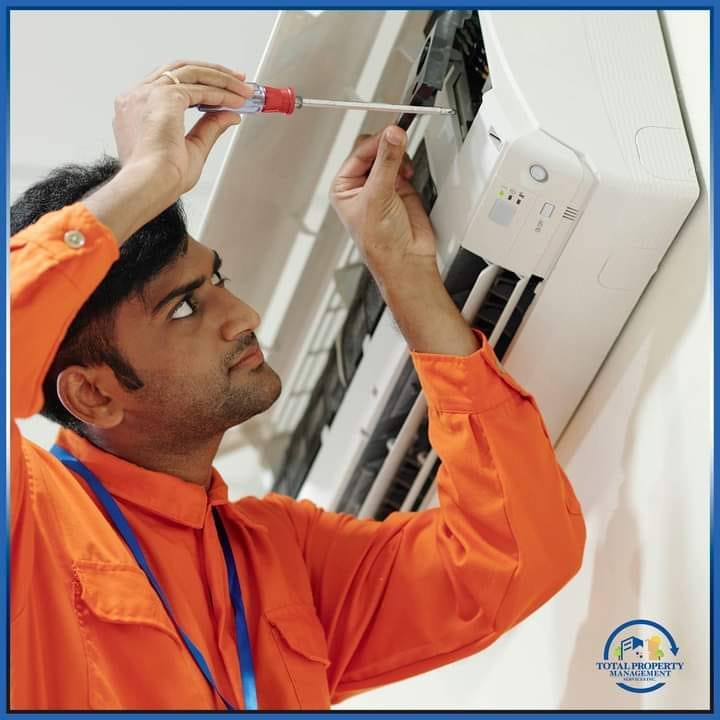 Technician in orange uniform using a screwdriver to repair an air‑conditioning unit, showcasing Total Property Management’s comprehensive maintenance services in Guyana.